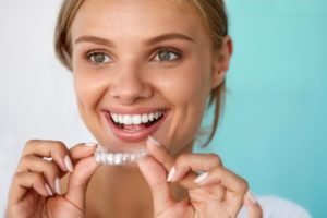 A woman holding a clear aligner and smiling.